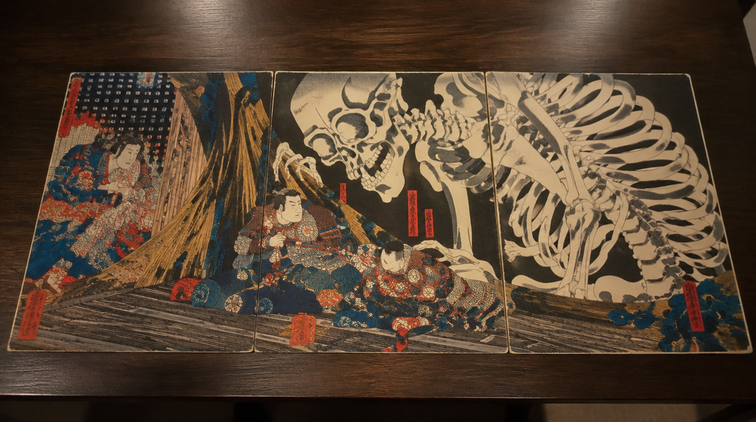 A Japanese triptych woodblock print of a giant skeleton spectre and warriors laid on a dark wooden table