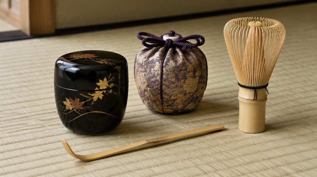 Japanese tea ceremony utensils: a black lacquer natsume, a bamboo tea scoop, a ceramic caddy in a silk pouch and a bamboo whisk on tatami
